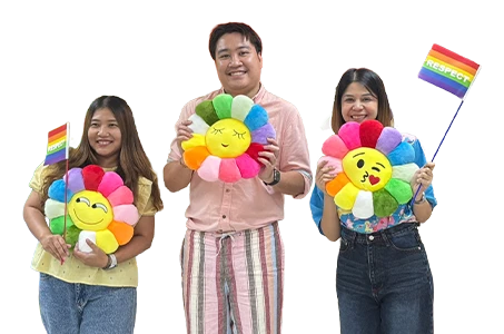 Two women and one man holding three colorful flower-shaped cushions and two rainbow flags (Photo)